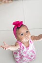 Zenithal shot of a brown baby kneeling on the ground, raising hands for her mother to carry her