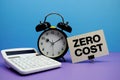 Zero Cost text with calculator and alarm clock on blue and purple background Royalty Free Stock Photo