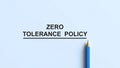 Zero Tolerance Policy text written in bold black font with a simple line underneath, next to a sharp blue pencil on a light blue Royalty Free Stock Photo