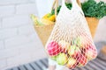 Zero waste concept with copy space. Woman holding straw basket and reusable mesh shopping bag withapples, vegetables, white brick Royalty Free Stock Photo