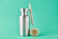 Zero waste concept. Eco friendly reusable aluminun bottle and wooden cleaning brush on a green background