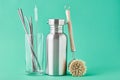 Zero waste concept. Eco friendly reusable items aluminun bottle and metal tubes in glass on a green background