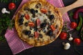 Flatbread pizza garnished with fresh arugula on wooden pizza board, top view. Dark stone background. Person picking slice of pizza Royalty Free Stock Photo