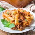 Ziti bolognese on a white plate, pasta casserole with minced meat, tomato sauce and cheese, square format