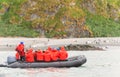 A Zodiac inflatable boat with Antarctic tourists in red parkas observes penguins on the coast of South Georgia