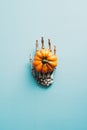Zombie hand holding pumpkin on blue background. Happy Halloween holiday poster design. Flat lay, top view, overhead Royalty Free Stock Photo