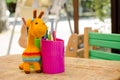 Zone for children entertainment in cafe. On outdoor terrace, colorful pencils, toy giraffe, and chair in glass on table.