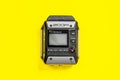 Zoom audio recorder with buttons and screen, laying on bright yellow background. Sound record equipment, close up.