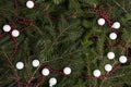 zoom on a pile of fir branches with a frame of bright red pearl garland and many christmas bauble red and white.