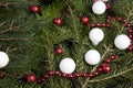 zoom on a pile of fir branches with a frame of bright red pearl garland and many christmas bauble red and white.