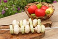 Zucchini and mushrooms on metal skewers on wooden chopping board with tomatoes, cucumber and bell pepper in a wicker basket