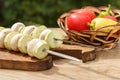 Zucchini and mushrooms on metal skewers on wooden chopping board with tomatoes, cucumber and bell pepper in a wicker basket