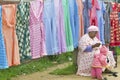 Zulu woman sewing garment in front of brightly colored dresses on display in Zulu village in Zululand, South Africa