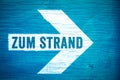 Zum Strand in German language, To the Beach text sign written on a white directional arrow on a blue wooden signboard Royalty Free Stock Photo