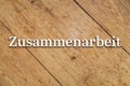 `Zusammenarbeit` white text on a wooden background. Translation: Cooperation