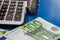 100 euro banknote, coins and part of the calculator on a blue background. Close-up.