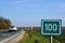 100 km milage sign along asphalt road. green field color and white lettering.