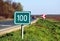 100 km milage sign along asphalt road. green field color and white lettering.