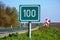 100 km milage sign along asphalt road. green field color and white lettering.