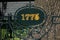 1775 year sign on metal forging fence in front of big tree. Information table placard or signboard in park or botanic garden to