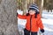 18 months baby hides behind tree in forest