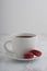 2 chocolate french macarons with a cup of coffee on a white marble table.