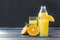 2 cups orange juice, bottle of juice, half orange, sprig of mint on a gray dark background