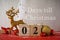 2 days before Christmas, a wooden calendar with a gold deer and decorations on a red-gray wood background. One of the 3 days of
