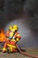 2 firemen spraying water in fire fighting with fire and dark smoke background