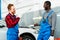 2 mechanics are laughing in front of white car after a difficult repair.