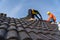 2 roofers working on the working at height to install the Concrete Roof Tiles on the new roof of new modern building construction