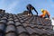 2 roofers working on the working at height to install the Concrete Roof Tiles on the new roof of new modern building construction