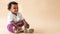 A 2-year-old Nigerian baby girl with beautiful curly hair, sitting on the floor, is smiling broadly