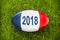 2018 written on a rugby ball in the grass, blue white red french flag colors