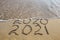 2020, 2021 years written on sandy beach sea. Wave washes away 2020