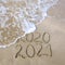 2020, 2021 years written on sandy beach sea. Wave washes away 2020