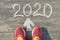 2020 arrow forward, written on gray sidewalk with woman legs in sneakers, top view