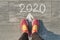 2020 arrow forward, written on gray sidewalk with woman legs in sneakers, top view