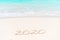 2020 handwritten on sandy beach with soft ocean wave on background