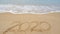 2020 Text on the beach, 2020 year message hand written in sand on beautiful beach Waves crashing on sandy shore background. New