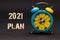 2021 plan written with alarm clock on black paper background