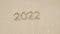 2022 hand write figures on sandy beach for Happy New Year 2023, The sea wave washes away number hand written on the golden beach