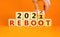 2022 reboot new year symbol. Businessman turns a wooden cube and changes words `Reboot 2021` to `Reboot 2022`. Beautiful orang