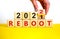 2022 reboot new year symbol. Businessman turns a wooden cube and changes words `Reboot 2021` to `Reboot 2022`. Beautiful white