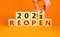 2022 reopen new year symbol. Businessman turns a wooden cube and changes words `Reopen 2021` to `Reopen 2022`. Beautiful orang