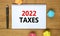 2022 taxes new year symbol. White note with words 2022 taxes on beautiful wooden table, colored paper, black metallic pen.