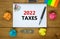 2022 taxes new year symbol. White note with words 2022 taxes on beautiful wooden table, colored paper, colored pencils, paper