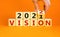 2022 vision new year symbol. Businessman turns a wooden cube and changes words `vision 2021` to `vision 2022`. Beautiful orang