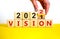 2022 vision new year symbol. Businessman turns a wooden cube and changes words `vision 2021` to `vision 2022`. Beautiful white