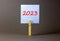 2023 happy new year symbol. Wooden clothespin, white sheet of paper with number 2023. Beautiful grey table grey background, copy